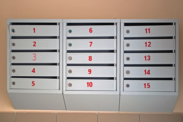 Painted gray mailboxes with keyholes with red apartment numbers on the doors hang on the beige wall of the entrance foyer at the entrance of a multi storey apartment building