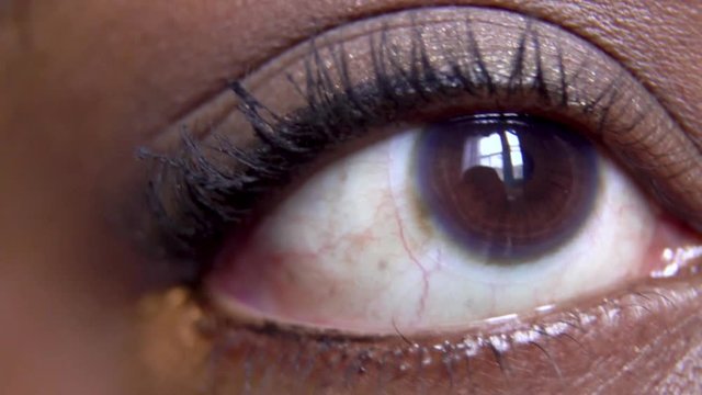 African American woman with brown eyes is applying mascara on her lashes in the soothing manner. the fine detail can be seen blinking slowly as she make herself pretty for the evening 