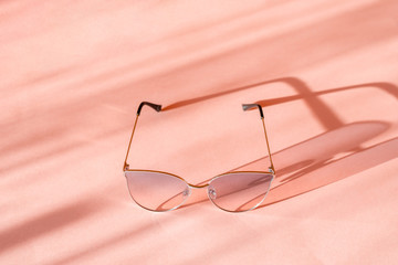 Women's pink sunglasses with metal frame cast a shadow on the pink surface. 