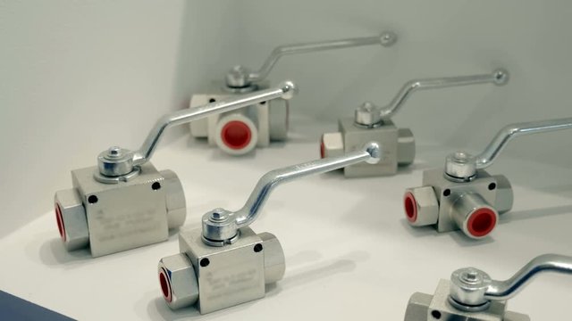 Shiny ball valves lie on a white surface. A new samples is presented for review at the exhibition. Shot in motion