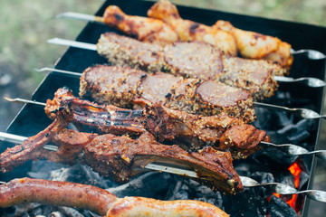 Summer barbecue with assortment of meat, meat mix, beef, spicy spare ribs and chicken legs grilling on the fire