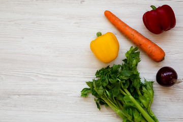 Fresh vegetables (carrot, celery, onion, colored peppers) on a white wooden surface, top view. From above, overhead, flat lay. Copy space.