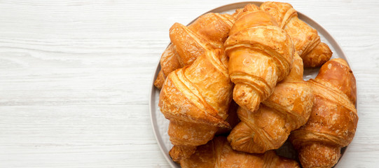 Freshly baked golden croissants on grey round plate on a white wooden background, overhead view. From above, top view, flat lay. Copy space.