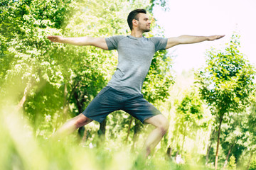 Male yoga relaxation. Sporty and slim handsome young man is doing yoga exercises in city park outdoors. Healthy lifestyle and strong soul and body