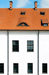 Fragment of a tiled roof and white facade of the castle with windows against the blue sky.