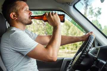 A man at the wheel holds a bottle of alcohol in his hand while driving, violates traffic rules. The...