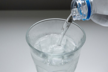 ガラスのグラスにペットボトルの水を注いでいるイメージ写真