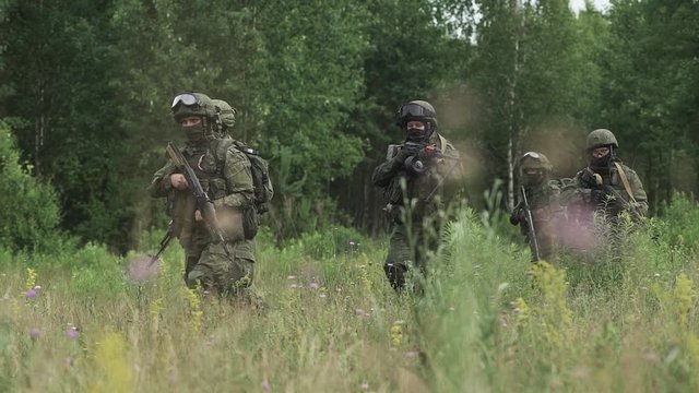 Soldiers in camouflage with assault rifle walking through the field military action in the steppe area.