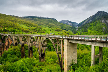 Montenegro, Old concrete building of durdevica tara bridge made of five arches leading traffic over impressive tara canyon in beautiful nature scenery - obrazy, fototapety, plakaty