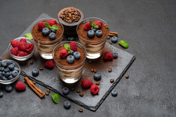 Classic tiramisu dessert with blueberries and raspberries in a glass on stone serving board on dark concrete background