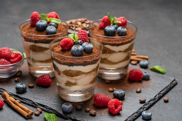 Classic tiramisu dessert with blueberries and raspberries in a glass on stone serving board on dark concrete background