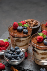 Classic tiramisu dessert with blueberries and raspberries in a glass on stone serving board on dark concrete background