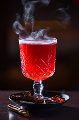 Hot cranberry drink with lemon, cinnamon and other spices on dark background