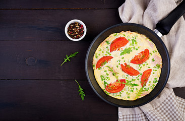 Omelette with tomatoes, ham and green onion on dark table.  Frittata - italian omelet. Top view