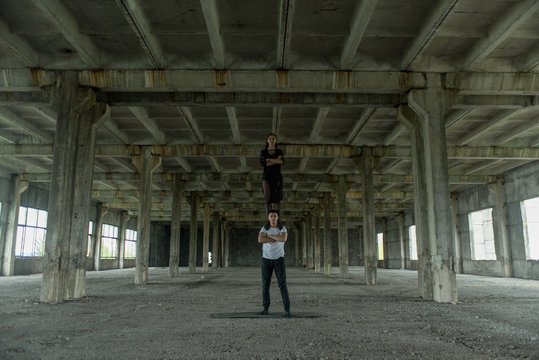 A young girl and boy perform acrobatic moves in the premises of an old factory, a warehouse, acro 