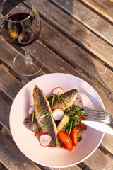 Fried mackerel fish with vegetable garnish: spinach in coconut milk, radish, onion and baked tomatoes, served on a sunny terrace with a glass of red wine