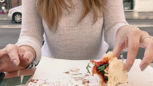 Slow motion shot of a woman with jewelry and painted fingernails and eats the last piece of arugula rucola pizza with balsamic sauce in outdoor restaurant near street