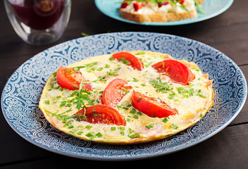 Omelette with tomatoes, ham and green onion on dark table.  Frittata - italian omelet.