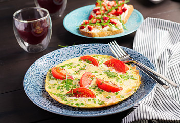 Omelette with tomatoes, ham and green onion on dark table.  Frittata - italian omelet.