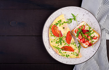 Omelette with tomatoes, ham, green onion and sandwich with strawberry on dark table.  Frittata - italian omelet. Top view