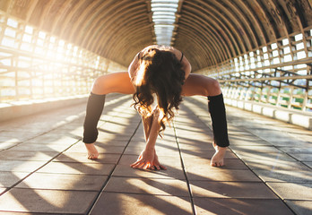 Slender young brunette woman street dancer gymnast sits in splits pose on street bridge at sunrise
