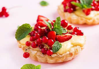 Tarts with strawberries, currant and whipped cream decorated with mint leaves.