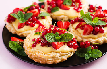 Tarts with strawberries, currant and whipped cream decorated with mint leaves.