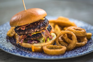 Tasty grilled burger with beef, tomato, cheese, cucumber and onion rings.