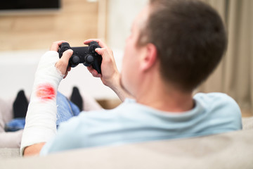 Man with broken arm in plaster cast with red blood play and holding controller in front of TV. Game addiction concept.