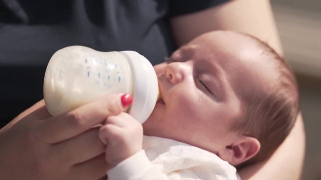 Young beautiful mother is feeding her little baby with a bottle of a milk .