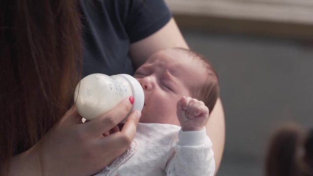 Young beautiful mother is feeding her little baby with a bottle of a milk .