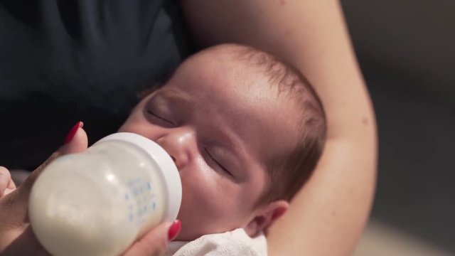 Young beautiful mother is feeding her little baby with a bottle of a milk .