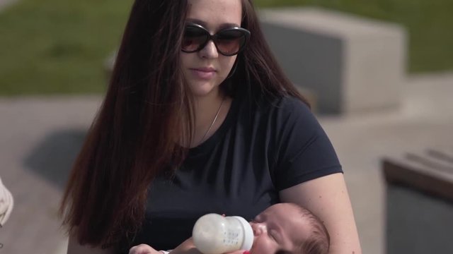 Young beautiful mother is feeding her little baby with a bottle of a milk .
