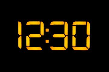 Electronic digital clock with yellow numbers on a black background shows the time Twelve thirty o'clock of the day. Isolate, close-up.