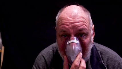 A mature aged balding man breathing with an oxygen mask.