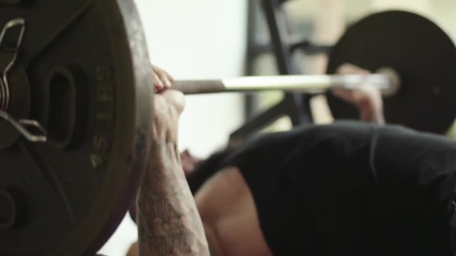 Sporty young man with tattoos lifting weight on bench press