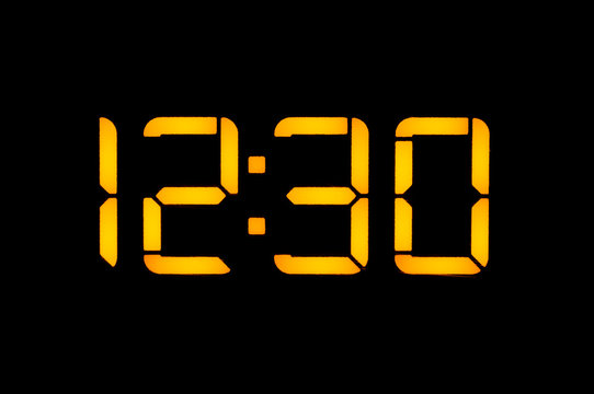 Electronic digital clock with yellow numbers on a black background shows the time Twelve thirty o'clock of the day. Isolate, close-up.