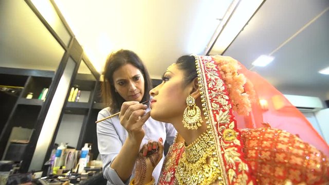 Beauty Salon Master doing makeup and applying red lipstick to beautiful asian girl. Wide Shot.