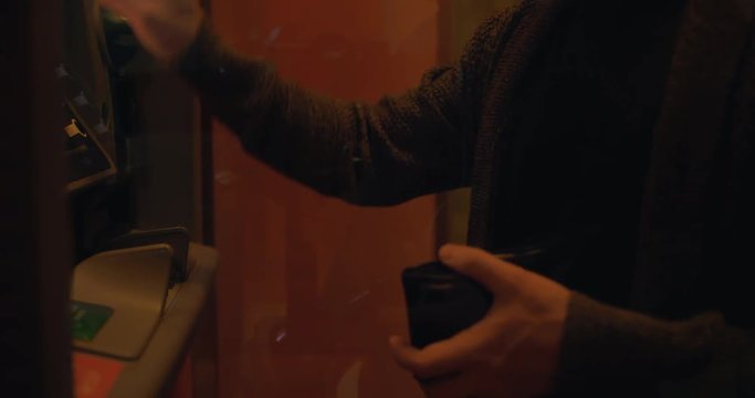 A man performs actions near the ATM. In his hand a wallet.