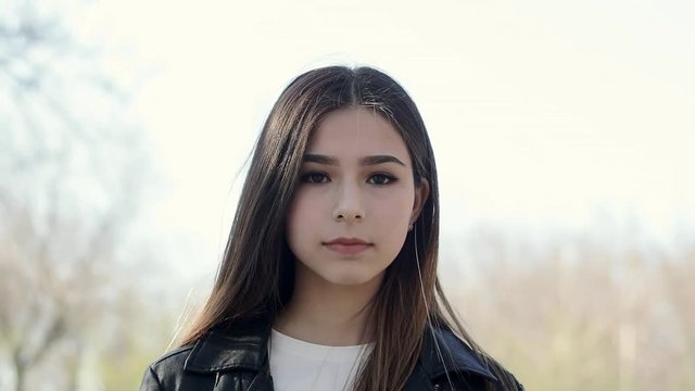 Serious teenage Asian mixed-race brunette girl outdoor. Portrait of a beautiful ethnic girl looking at camera closeup.