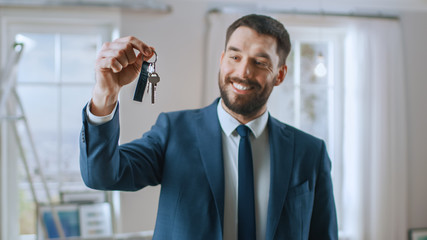 Successful Real Estate Agent in a Suit Smiles and Offers Keys From a New Apartment. Standing in the...