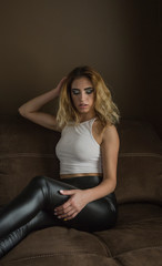 Fototapeta na wymiar Sensual woman in white top and black leather trousers posing in dark interior