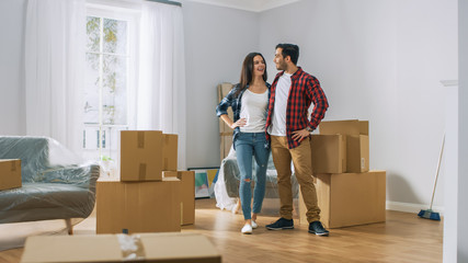 Happy Young Couple Moving Into New Apartment, Carrying Cardboard Boxes with Stuff and Poses on...