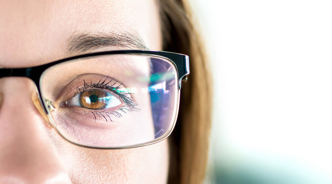 Close up of eye and woman wearing glasses. Optometry, myopia or laser surgery concept. Brown eyed girl with spectacles and eyeglasses. Macro portrait of face and specs. Light reflection on lens.