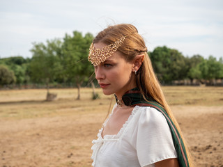 Close-up of blonde girl with blue eyes and elf ears wearing a green cape