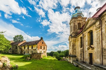 Naklejka premium Skoky, Zlutice / Czech Republic - June 21 2019: Baroque church of the Virgin Mary Visitation in Skoky, Maria Stock, former pilgrimage place in West Bohemia. Sunny day, blue sky and clouds. Ruin house.