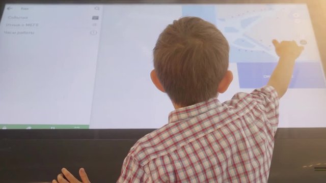 Child is using a touch screen of interactive information stand in the supermarket.