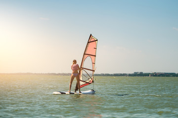 Young athletic slim girl sails on a windsurf board in the open sea on summer vacation at resort. Windsurfing