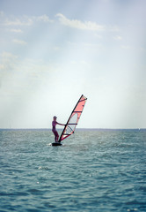 Young athletic slim girl sails on a windsurf board in the open sea on summer vacation at resort. Windsurfing