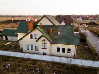 Aerial view of new residential house cottage and garage or barn with shingle roof on fenced yard on sunny day.